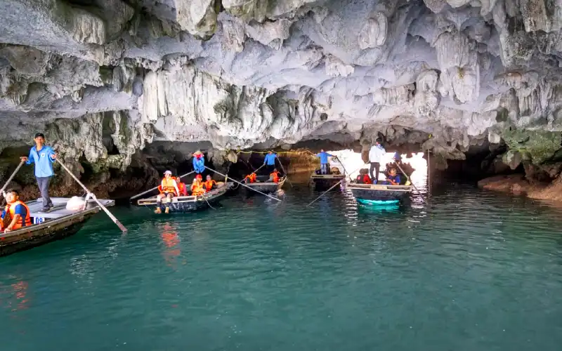 Wooden rowboat entering a natural low-hanging river cave system in Trang An