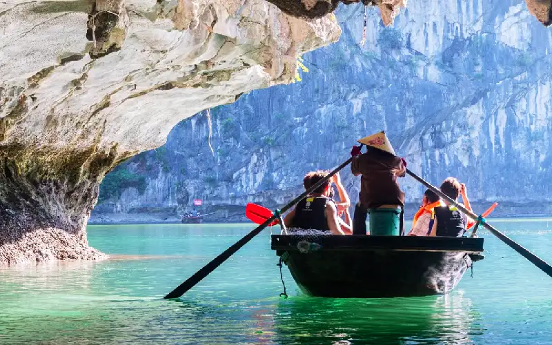 Inside-the-Hidden-Caves-of-Ha-Long Tourists explore a picturesque cave in Ha Long Bay, Vietnam, featuring crystal-clear turquoise waters and majestic limestone formations.